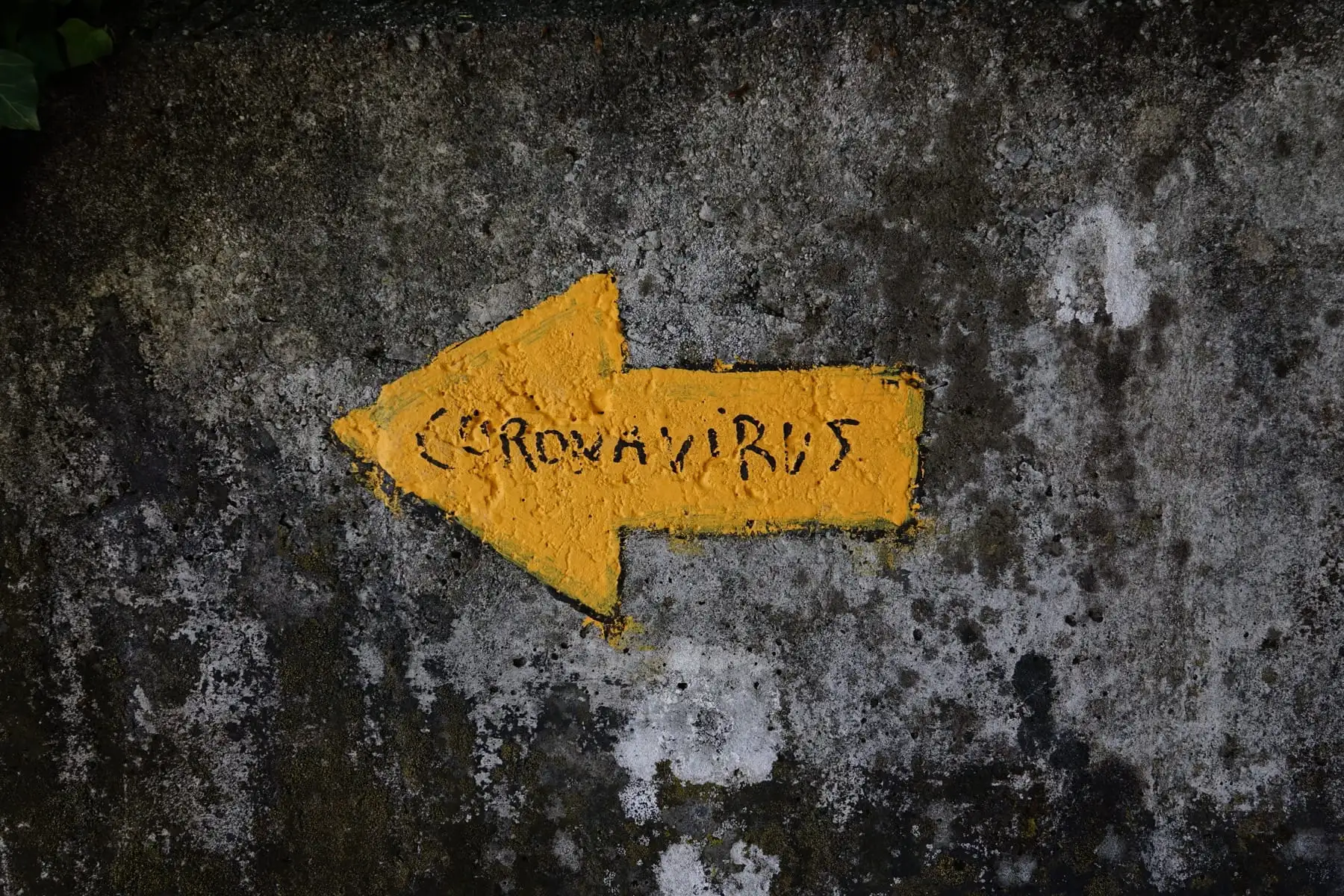 A yellow arrow with coronavirus written inside, painted on an old wall